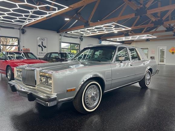 1985 Chrysler New Yorker — silver with white wall tires in showroom